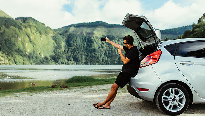 Image of a guy with his car somewhere in the mountains taking a selfie